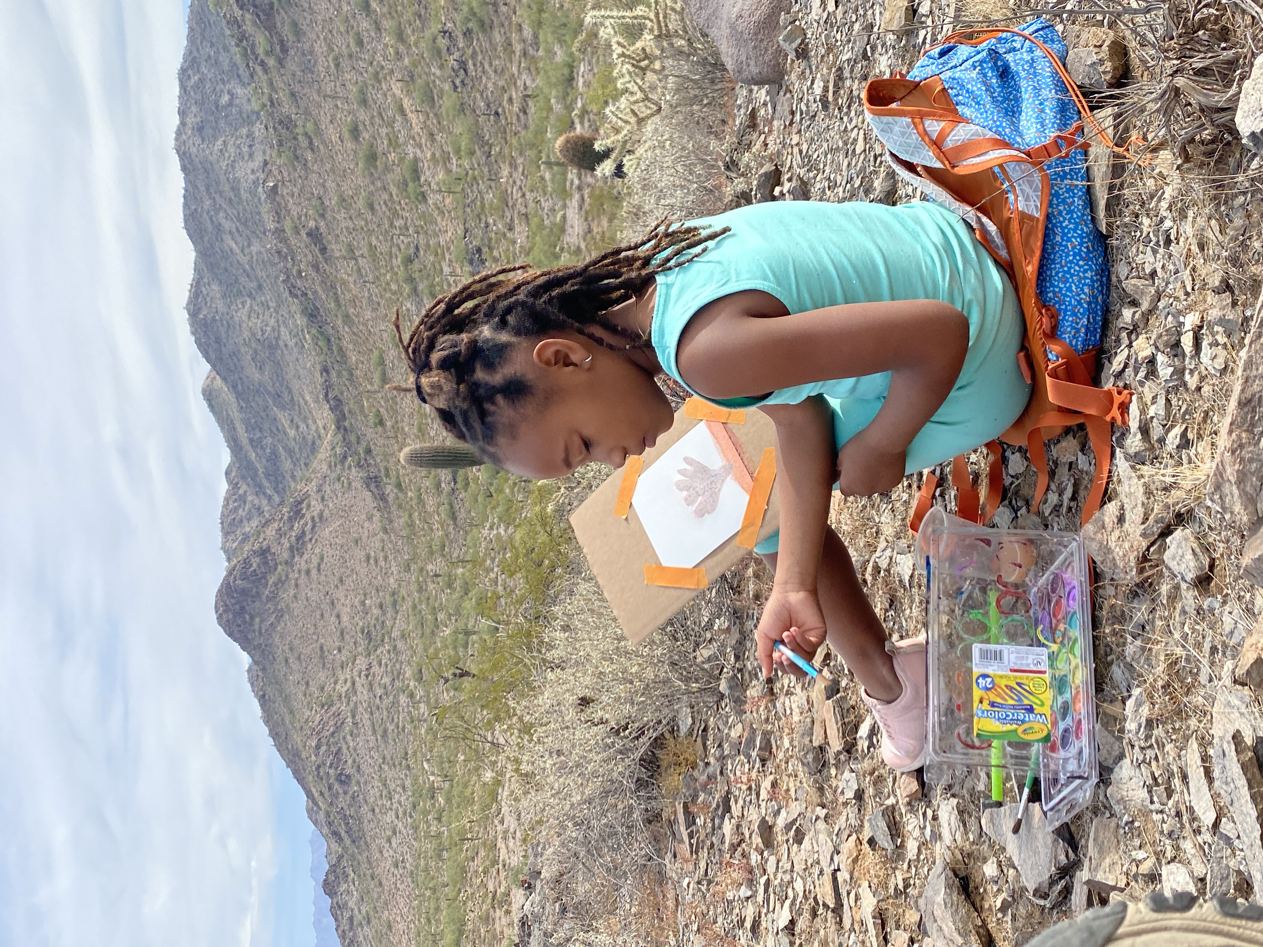 A young girl sits in front of a desert landscape painting